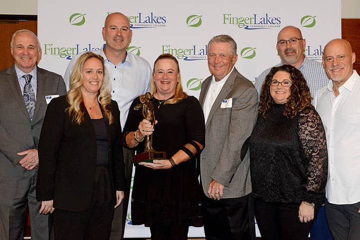 Distinguished Alumni Award winner with trophy in hand stands with FLCC staff.