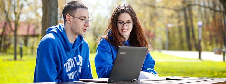 Two students streaming a club event on their laptop.