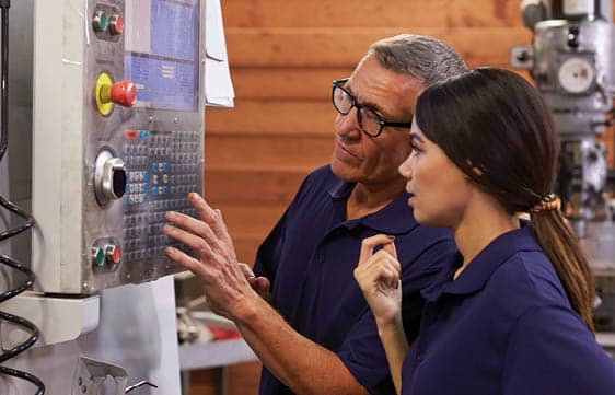 Two individuals working at a machine operating control panel.