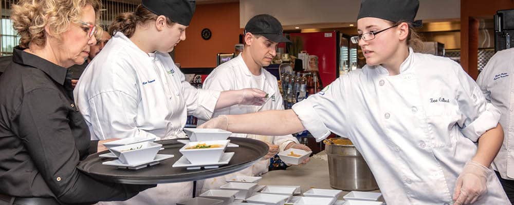 A group of Culinary Arts students in white chef's jackets dishing up soup for an event.