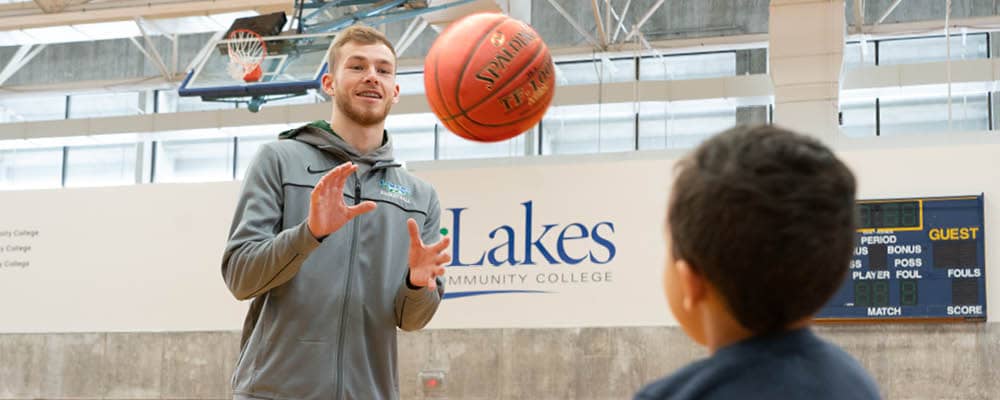 A Physical Education and Exercise Science student tossing a basketball with a grade-school student in the FLCC gymnasium